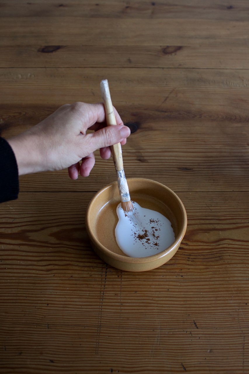 mano mezcla con un pincel en un recipiente pintura blanca con polvo de arcilla